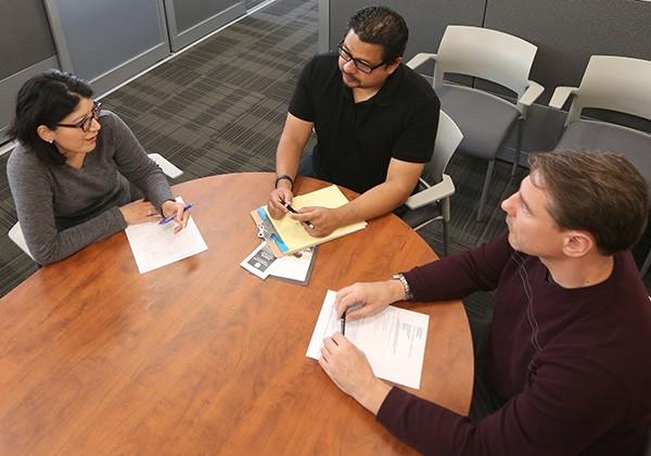 3 people sitting around table, evaluating paperwork