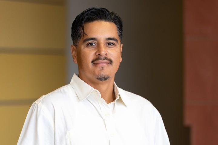 Gregorio Pacheco wearing a white cream colored dress shirt in front of a yellow wall