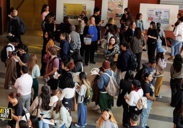 A busy event with people standing and reviewing poster presentations in an open indoor space